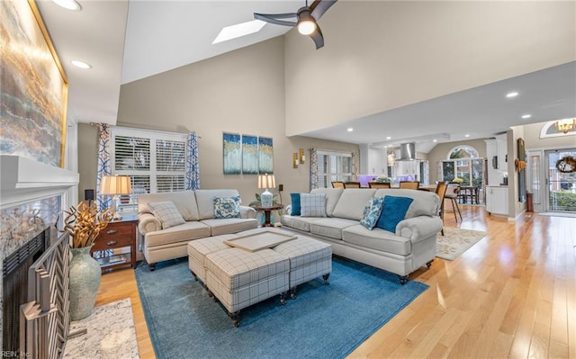 living room with ceiling fan, high vaulted ceiling, a skylight, and light hardwood / wood-style floors