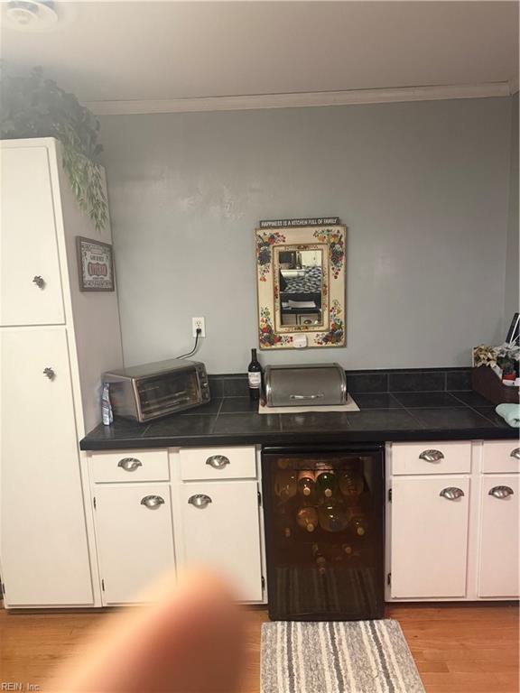 kitchen featuring white cabinetry, ornamental molding, wine cooler, and light wood-type flooring