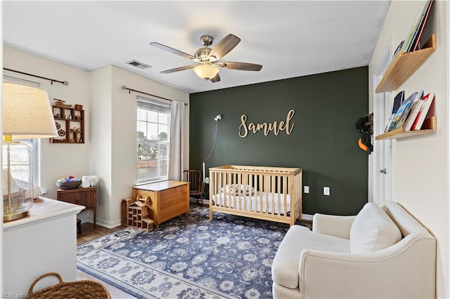 bedroom with hardwood / wood-style floors, a crib, and ceiling fan