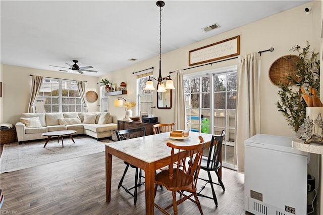 dining area featuring ceiling fan with notable chandelier and wood-type flooring