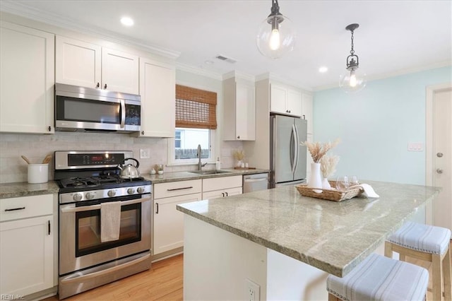 kitchen featuring appliances with stainless steel finishes, pendant lighting, sink, white cabinets, and a kitchen bar