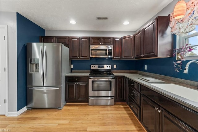 kitchen with appliances with stainless steel finishes, sink, dark brown cabinets, and light hardwood / wood-style flooring