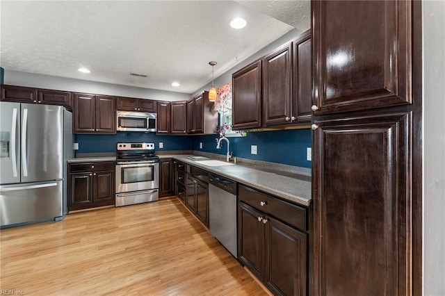 kitchen featuring pendant lighting, sink, dark brown cabinets, stainless steel appliances, and light hardwood / wood-style floors