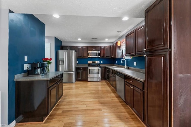 kitchen with decorative light fixtures, sink, dark brown cabinetry, stainless steel appliances, and light wood-type flooring