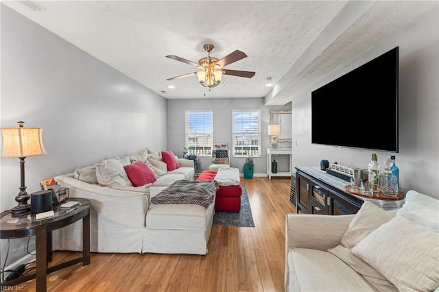 living room with a textured ceiling, ceiling fan, and light wood-type flooring