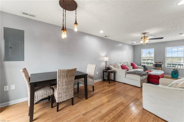 dining room featuring a textured ceiling, light hardwood / wood-style flooring, electric panel, and ceiling fan