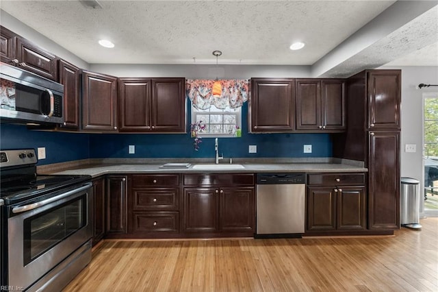 kitchen featuring appliances with stainless steel finishes, decorative light fixtures, sink, a textured ceiling, and light hardwood / wood-style flooring