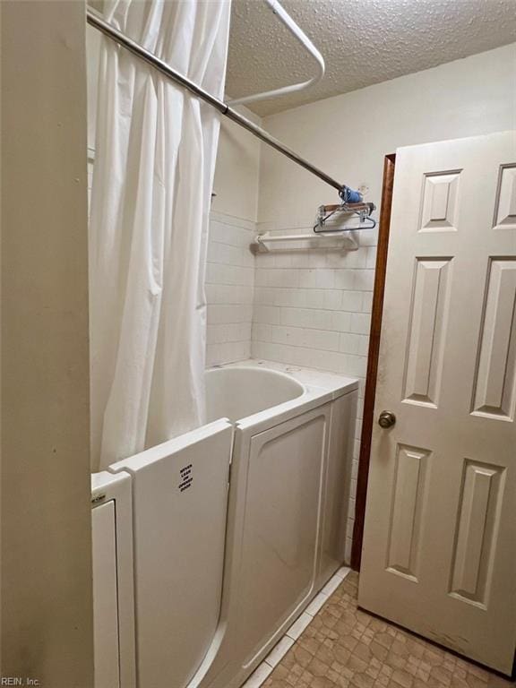 bathroom with tile walls, shower / bathtub combination with curtain, and a textured ceiling