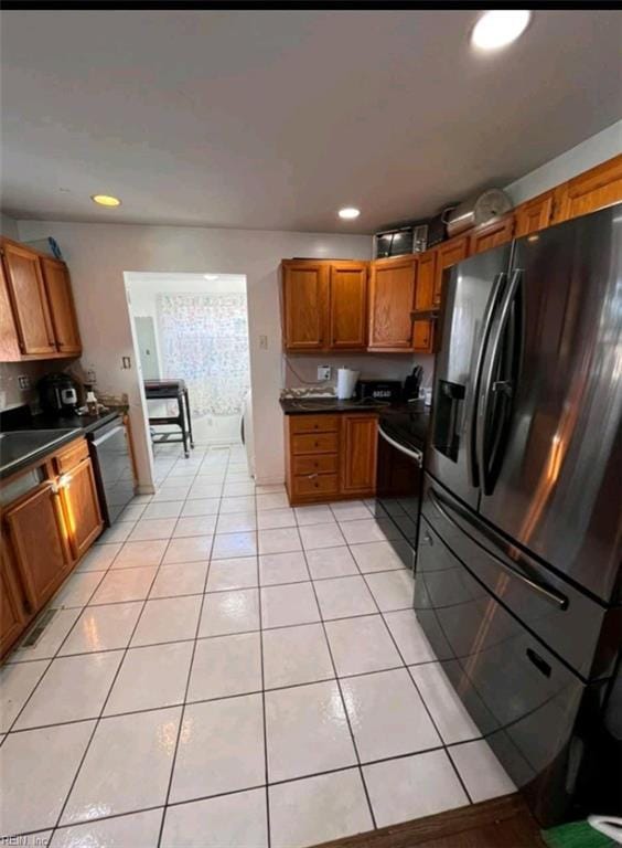 kitchen with dark countertops, light tile patterned floors, brown cabinetry, and black fridge