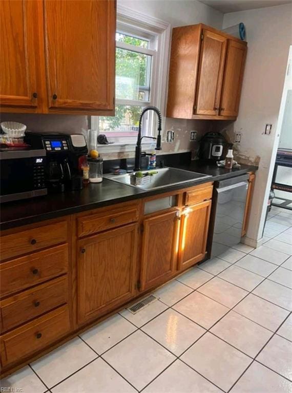 kitchen with dishwasher, dark countertops, a sink, and brown cabinets