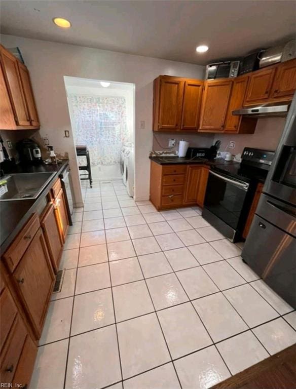 kitchen with black electric range, brown cabinets, dark countertops, separate washer and dryer, and under cabinet range hood