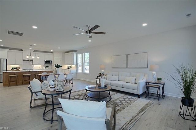 living room with ceiling fan, sink, and light hardwood / wood-style floors