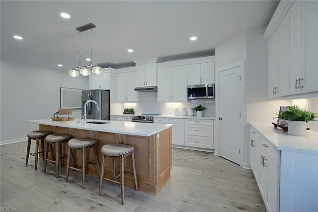 kitchen featuring white cabinetry, stainless steel appliances, an island with sink, and pendant lighting