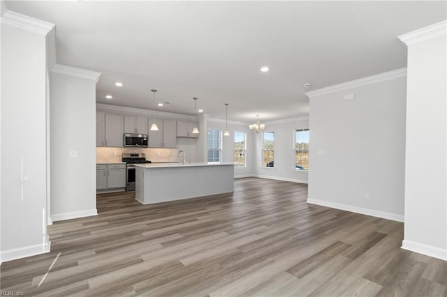 kitchen featuring appliances with stainless steel finishes, an island with sink, gray cabinetry, decorative backsplash, and hanging light fixtures