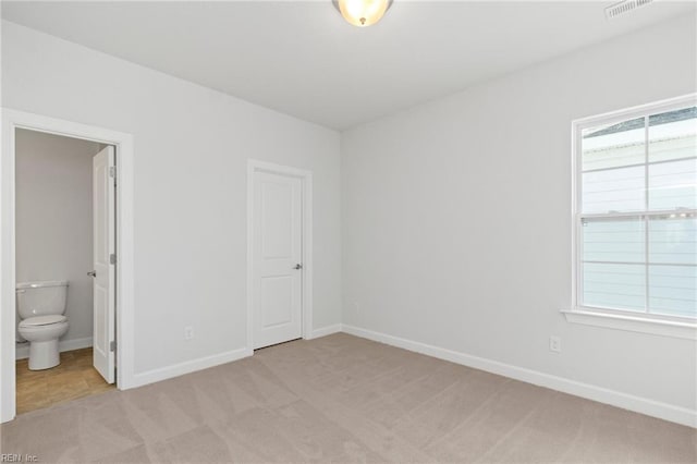 unfurnished bedroom with multiple windows, ensuite bathroom, and light carpet