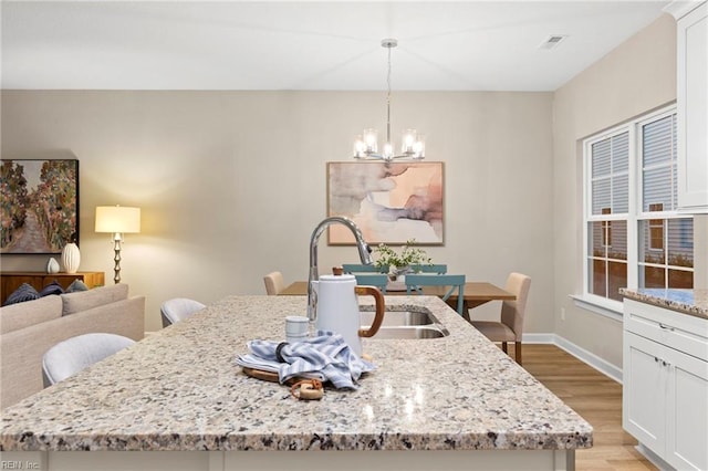 kitchen featuring a kitchen bar, hanging light fixtures, a kitchen island with sink, light stone counters, and light hardwood / wood-style flooring