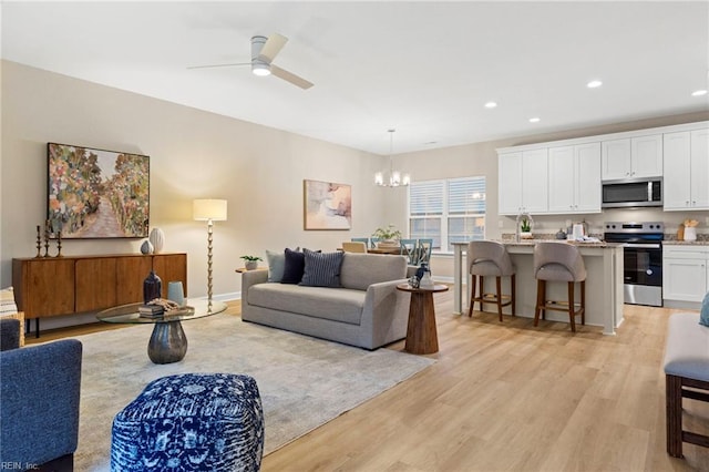 living room featuring ceiling fan with notable chandelier and light hardwood / wood-style floors