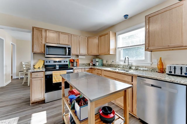 kitchen with appliances with stainless steel finishes, light brown cabinetry, sink, light stone counters, and light hardwood / wood-style flooring