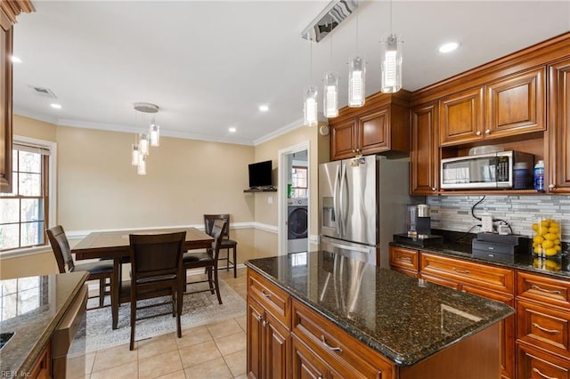 kitchen with appliances with stainless steel finishes, hanging light fixtures, a center island, decorative backsplash, and washer / dryer