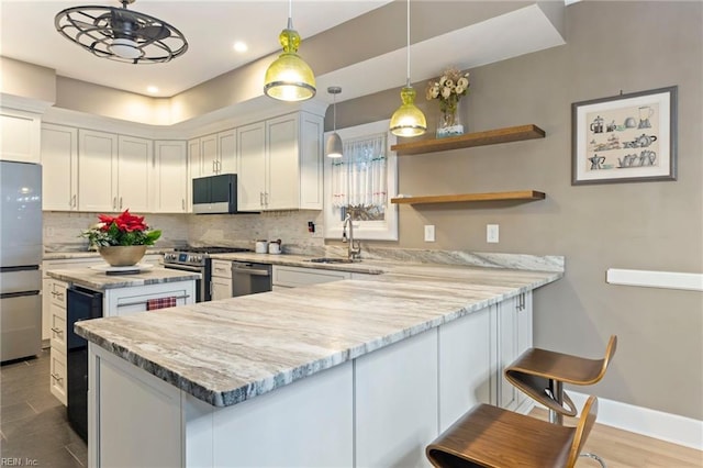 kitchen featuring a breakfast bar, sink, white cabinetry, appliances with stainless steel finishes, and light stone countertops