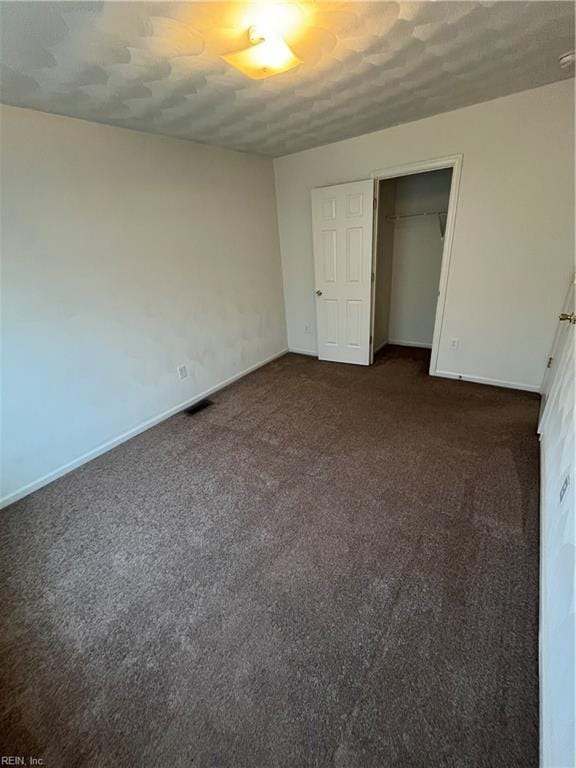 unfurnished bedroom with a textured ceiling, a closet, and dark colored carpet