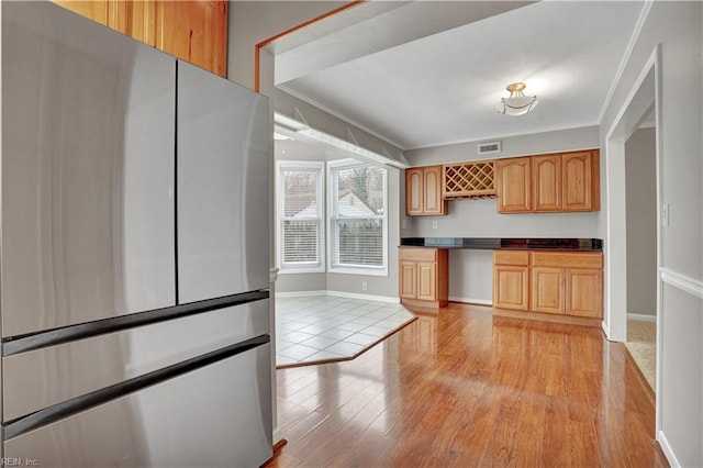 kitchen featuring ornamental molding, stainless steel fridge, light brown cabinetry, and light hardwood / wood-style flooring