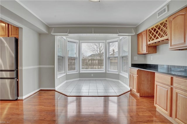 kitchen featuring light brown cabinetry, ornamental molding, light hardwood / wood-style floors, and stainless steel refrigerator