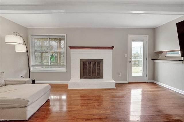 unfurnished living room featuring hardwood / wood-style floors, ornamental molding, and a brick fireplace