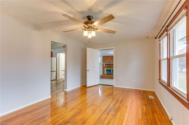 spare room with ceiling fan, a fireplace, hardwood / wood-style floors, and a textured ceiling