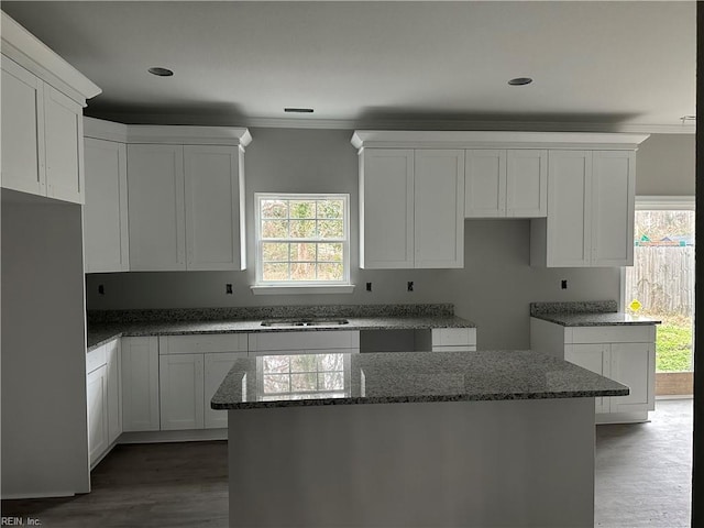 kitchen with hardwood / wood-style floors, white cabinets, dark stone counters, ornamental molding, and a center island