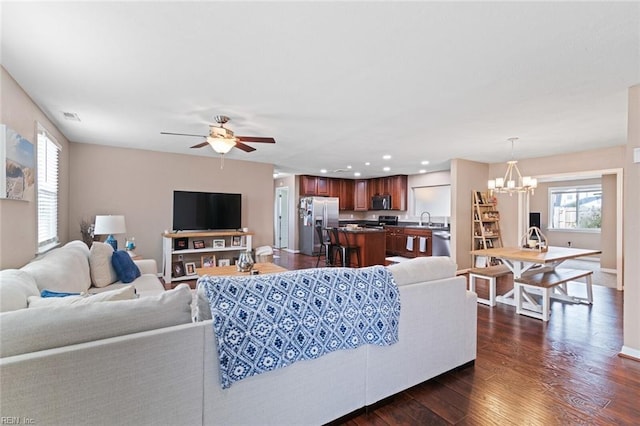 living room with ceiling fan with notable chandelier, dark hardwood / wood-style flooring, and sink