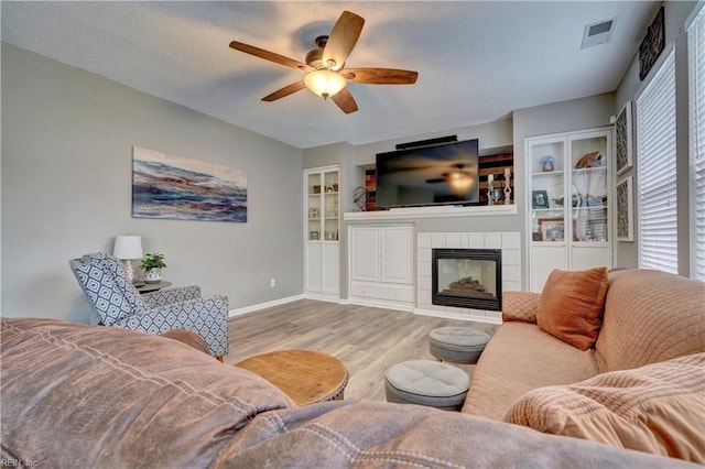 living room featuring a textured ceiling, light wood-type flooring, built in features, ceiling fan, and a fireplace