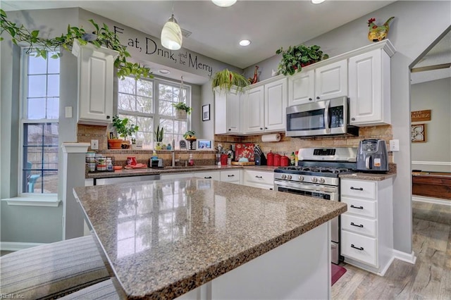 kitchen with appliances with stainless steel finishes, a center island, light stone counters, white cabinets, and decorative light fixtures