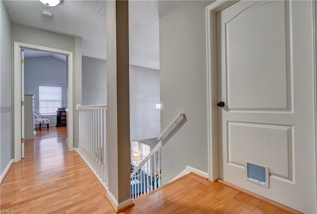 hall with vaulted ceiling, light hardwood / wood-style flooring, and a textured ceiling