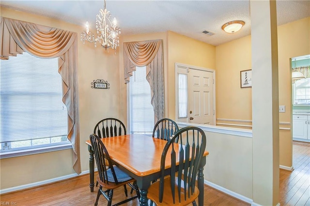 dining area with plenty of natural light, an inviting chandelier, a textured ceiling, and light hardwood / wood-style floors