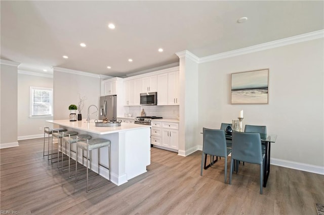 kitchen featuring appliances with stainless steel finishes, a center island with sink, white cabinets, and a kitchen breakfast bar