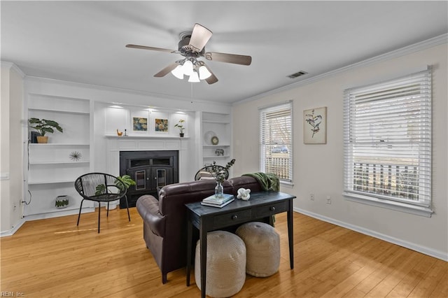 living room with crown molding, ceiling fan, built in features, and light wood-type flooring