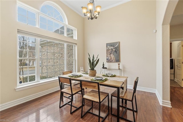 dining space featuring dark hardwood / wood-style floors, washer / clothes dryer, a high ceiling, crown molding, and an inviting chandelier