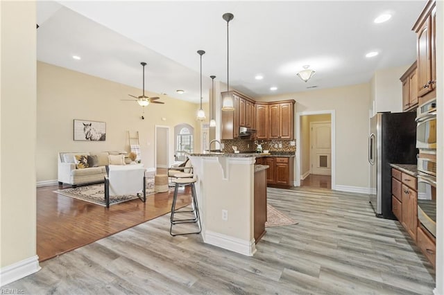 kitchen featuring appliances with stainless steel finishes, stone countertops, a kitchen breakfast bar, decorative backsplash, and light hardwood / wood-style flooring