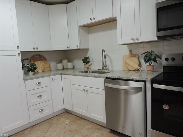 kitchen with sink, appliances with stainless steel finishes, white cabinetry, light stone counters, and tasteful backsplash