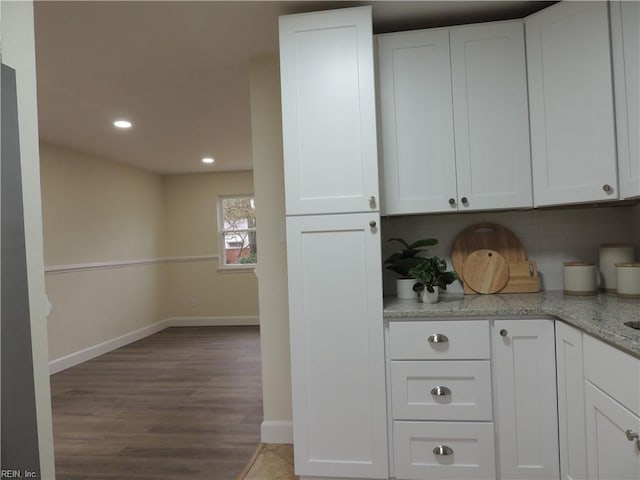 kitchen with white cabinetry, wood-type flooring, light stone countertops, and backsplash