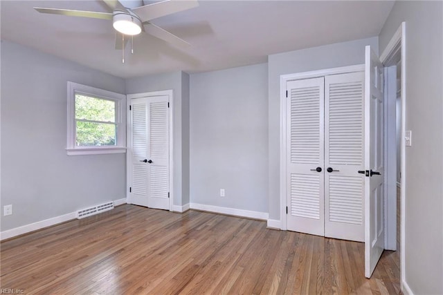 unfurnished bedroom featuring ceiling fan, light wood-type flooring, and two closets