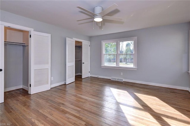 unfurnished bedroom featuring multiple closets, ceiling fan, and wood-type flooring