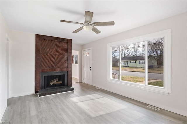 unfurnished living room featuring a brick fireplace, ceiling fan, and light wood-type flooring