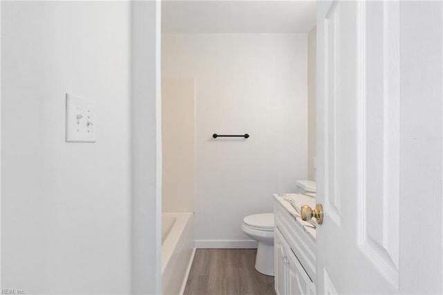 bathroom with hardwood / wood-style flooring, a tub to relax in, vanity, and toilet