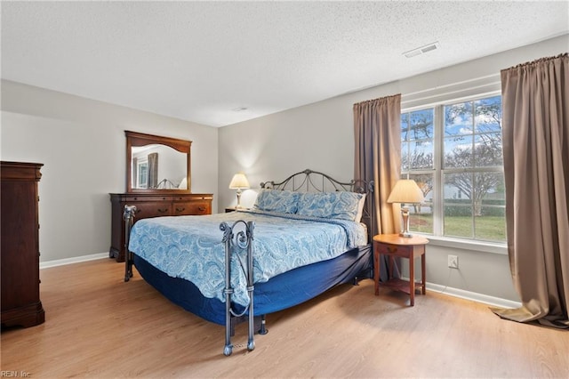 bedroom with multiple windows, a textured ceiling, and light hardwood / wood-style floors