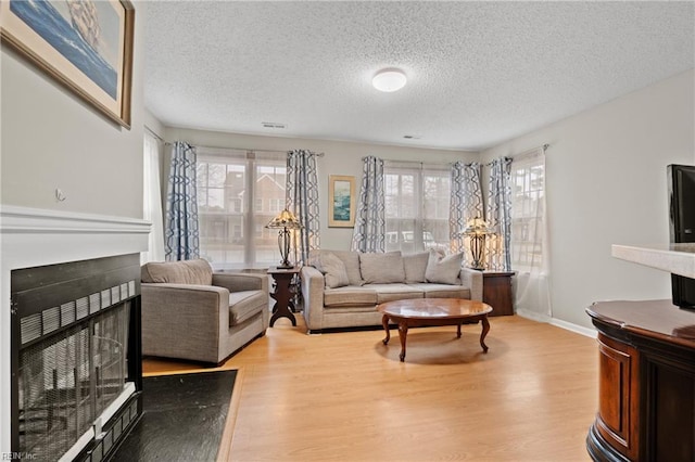 living room featuring light wood-type flooring, a textured ceiling, and a multi sided fireplace