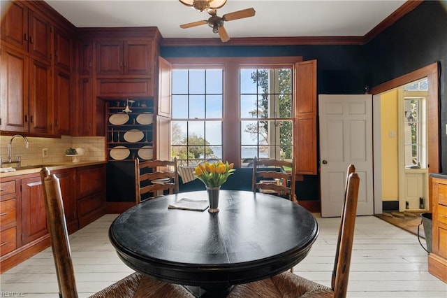 dining space with ornamental molding, plenty of natural light, sink, and light hardwood / wood-style flooring