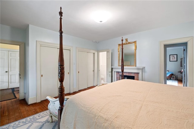 bedroom with multiple closets, ensuite bath, wood-type flooring, and a fireplace