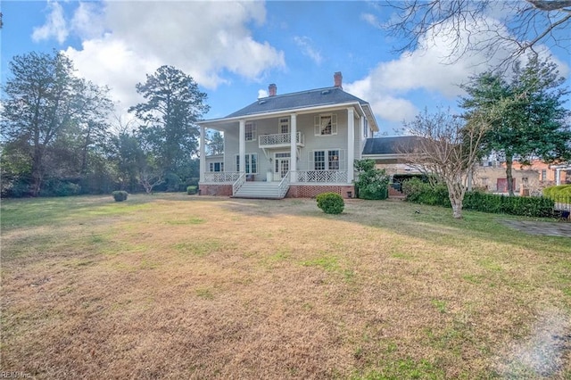 rear view of house with a yard, a balcony, and covered porch